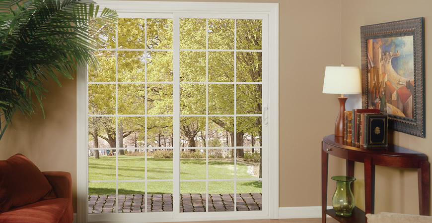 White sliding patio door with divided-light grids opening to a green backyard